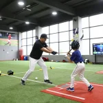 Hitclub baseball training session with coach guiding young athlete in a dynamic sports facility.