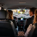 Taxi Amsterdam interieur met vriendelijke chauffeur en tevreden passagiers die genieten van een soepele rit door de stad.